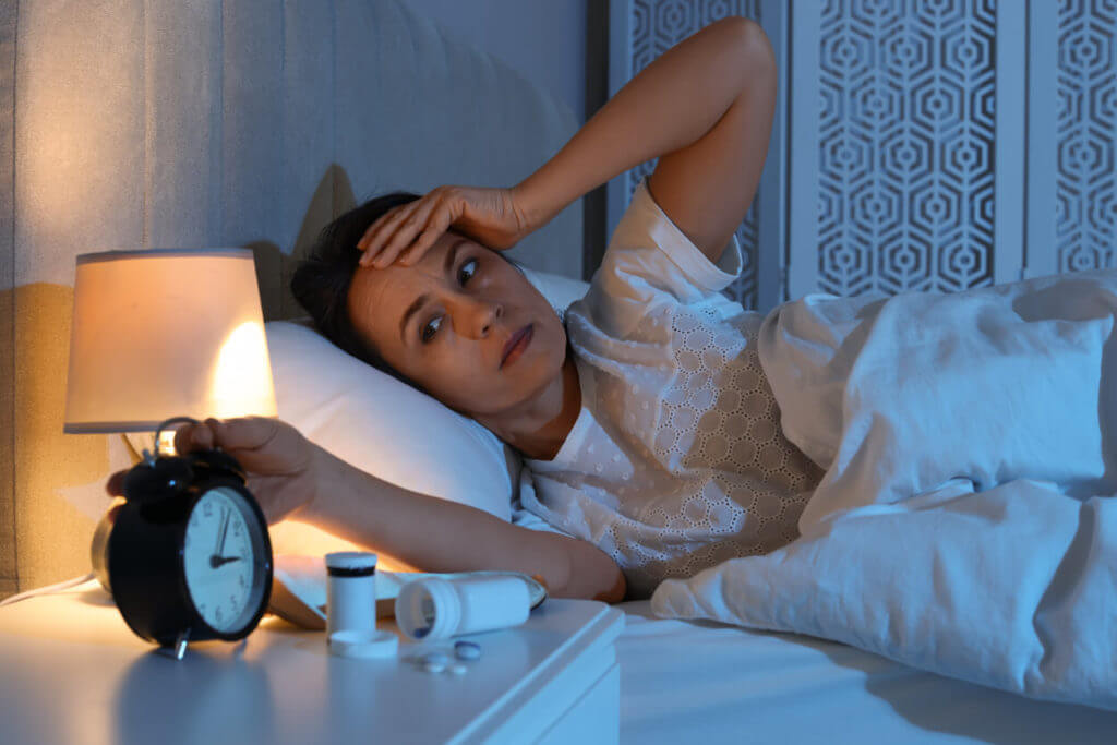 A mature woman is suffering from insomnia in bed at night due to poor sleep hygiene.