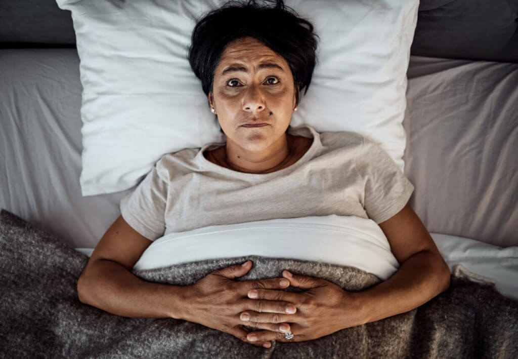 A senior woman in bed while struggling to fall asleep or stay asleep due to Insomnia.