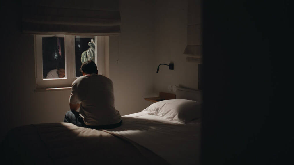 A sad man sitting bed home looking window feeling lonely and with insomnia.