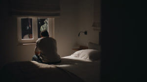 A sad man sitting bed home looking window feeling lonely and with insomnia.